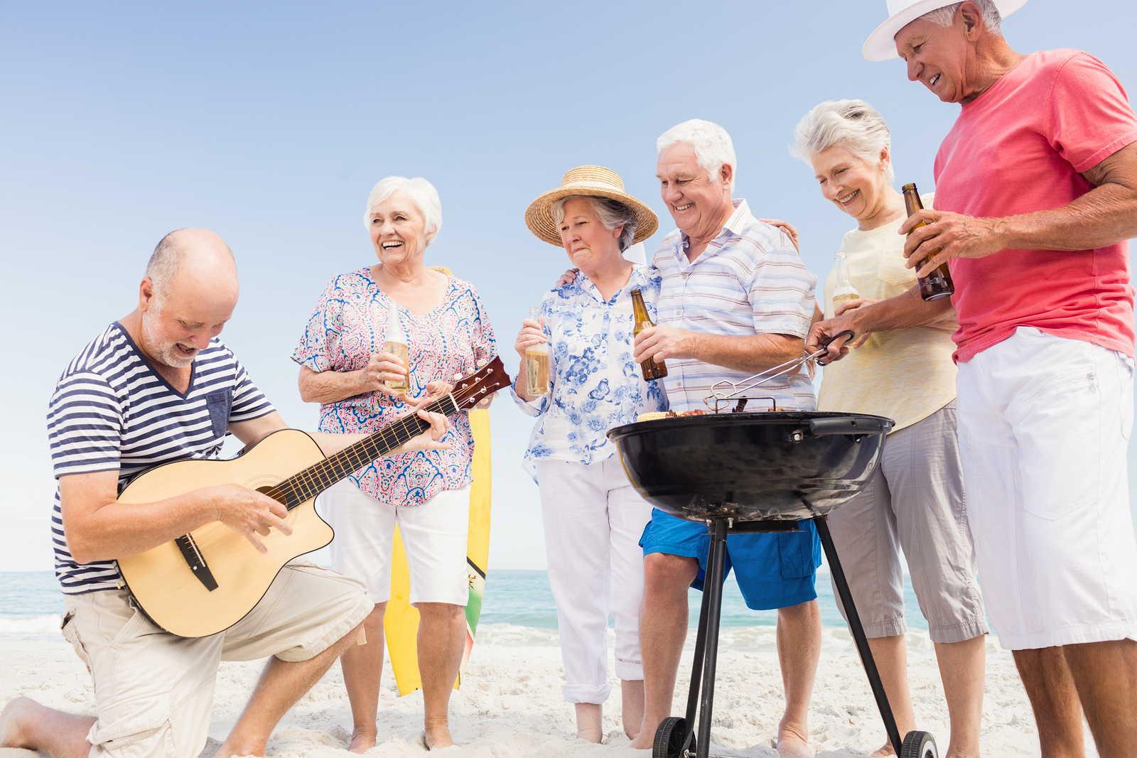 Seniors at a beach singing and one is playing a guitar