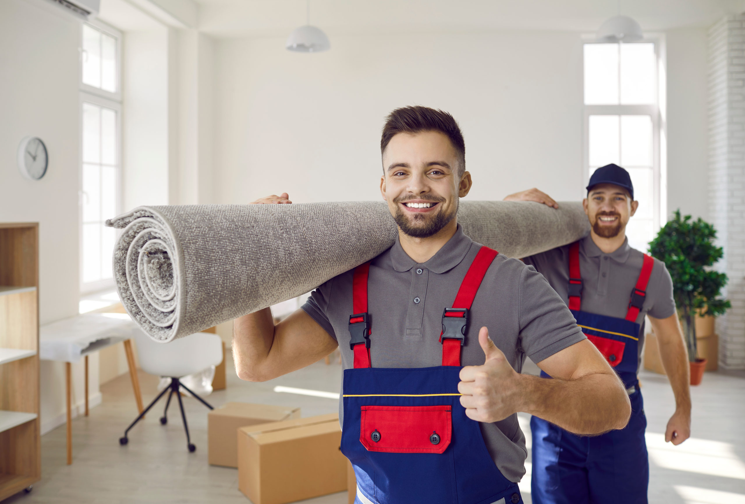 smiling male movers carry carpet with 1st mover giving a thumbs up